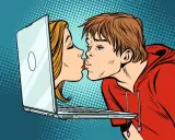 Chłopak i dziewczyna całują się przez ekran laptopa, symbolizując cyber sex i wirtualną bliskość.