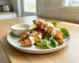 Krispiga bitar av panerad kyckling serveras på en bädd av sallad med krämig dressing och parmesan. En perfekt lunch eller middag.