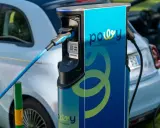 Estación de recarga para coche eléctrico con cable azul conectado. La estación tiene el logo "powy" y el lema "CHARGE THE CHANGE".