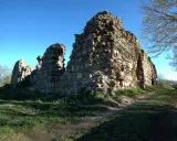 Kamienne ruiny zamku w Kurzętniku, porośnięte trawą, stoją na wzgórzu pod błękitnym niebem.