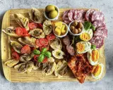 Ein köstlicher Antipasti-Abend mit Bruschetta, Sardellen, Tomaten, Oliven, Käse, Eiern und Salami auf einem Holzbrett.