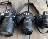 Trzy aparaty Canon EOS R, RP i R5 z obiektywami leżą obok siebie. Pełna klatka w całej okazałości.