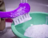 Fioletowa szczoteczka z pastą z sody i wody utlenionej nad zieloną miseczką z proszkiem.