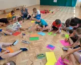 Dzieci i dorośli siedzą na podłodze, rysując i malując. To świetne pomysły na integrację zespołu klasowego, rozwijające kreatywność i współpracę.