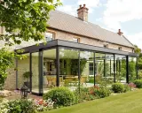 Maison en pierre avec extension moderne, une véranda lumineuse avec cuisine et salle à manger, entourée d'un jardin fleuri.