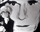 Andy Warhol, Ikone der Pop Art, posiert vor einem riesigen Porträt von sich selbst. Seine Kunstrichtung prägte die moderne Kunst.