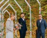 Piękna panna młoda z bukietem, pan młody przemawia do mikrofonu, a pan młody z uśmiechem. Wesele jesienią w otoczeniu kolorowych liści.
