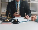 Prawnik wyjaśnia, jak zabezpieczyć się przed długami brata. Na stole waga sprawiedliwości, młotek sędziowski i dokumenty.