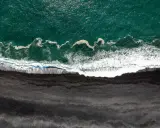 Gran Canaria: Türkisfarbenes Meer trifft auf einen dramatischen schwarzen Strand. Wellen brechen sich auf dem dunklen Sand.