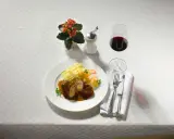 Ein Teller Rouladen mit Bandnudeln und einem Glas feinherb Wein. Dazu ein kleines Blümchen und Besteck.