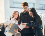 Trzech studentów dyskutuje nad notatkami, ich status ucznia widoczny w skupieniu i materiałach.