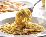 Pyszne dania z makaronem: spaghetti z ziołami i czosnkiem, na talerzu, z widocznym w tle pieczywem.