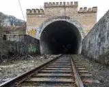 Torowisko prowadzi do ciemnego tunelu pod ceglanym łukiem z blankami, przypominającym bramę do dawnej kopalni Rydułtowy.