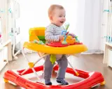 Uśmiechnięty maluch w chodziku bawi się zabawkami. Od kiedy chodzi, świat jest dla niego jeszcze ciekawszy!