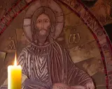 Płonąca świeca przed płaskorzeźbą Chrystusa, symbolizująca modlitwę o spokój i wyciszenie.