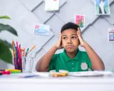 Niño frustrado con las manos en la cabeza, rodeado de materiales de arte, quizás lidiando con problemas de aprendizaje.