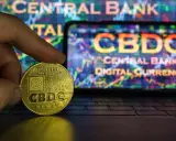 Złoty żeton CBDC w dłoni, symbolizujący cyfrowy pieniądz w Polsce. W tle ekran z wykresem i napisem "CENTRAL BANK DIGITAL CURRENCY".