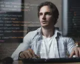 Mężczyzna pracuje nad kodem, tworząc aplikację full stack. W tle widać fragmenty kodu HTML i JavaScript.