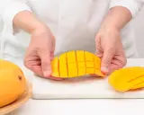 Ręce trzymają pokrojone w kostkę mango, pokazując, jak pokroić mango. Obok leżą całe owoce.