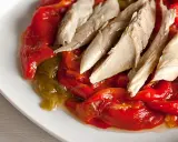 Pimientos asados rojos y verdes con trozos de pescado blanco encima, servidos en un plato blanco.