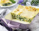 Pyszne lasagne ze szpinakiem w fioletowym naczyniu, gotowe do podania. Obok talerze z porcją i sztućce.