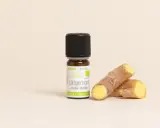 Flacon d'huile essentielle de gingembre bio, aux côtés de morceaux de rhizomes frais. Un concentré de vitalité.