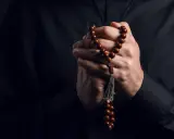 Dłonie księdza trzymające paciorki różańca, symbol wiary i nadziei w obliczu trudów życia, gdzie pańszczyzna a kościół splatały się w historii.