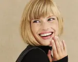 Frau mit blondem Bob, die lacht und ihre Hand vor den Mund hält. Perfekt gestylter Bob.