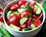 Frischer Tomaten-Gurken-Salat mit roten Zwiebeln und Petersilie, garniert mit ganzen Kirschtomaten und Gurken.