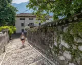 Una donna sale una scalinata di ciottoli verso un edificio bianco, un percorso che ricorda la salita alla Madonna della Corona.