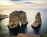 Felsformationen im Meer vor der Küste von Beirut Stadt, mit einem kleinen Boot, das durch den Felsbogen fährt.