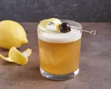 Ein erfrischender Amaretto Sour mit Zitronenzeste und Kirsche, daneben eine Zitrone.
