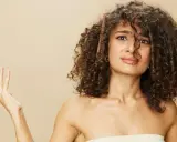 Une femme aux cheveux bouclés tente de diminuer le volume de sa chevelure avec un peigne.