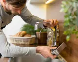 Hombre ajustando grifo de cocina para regular la presión del agua en casa.