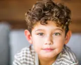 Ein Junge mit vollen, lockigen Haaren und grünen Augen lächelt sanft.