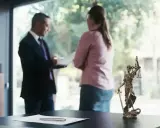 Mecenas, kto to? Prawnik w garniturze rozmawia z klientką przy biurku z figurką Temidy.