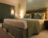 Ideas de iluminación para dormitorio de matrimonio: cama acogedora con lámparas de noche y cortinas verdes.