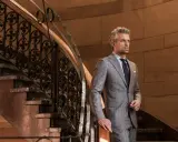 Elegancki mężczyzna w garniturze w kratę księcia Walii stoi przy ozdobnej klatce schodowej.