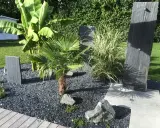 Une belle entrée de maison extérieure avec une plante luxuriante, des ardoises et un palmier.
