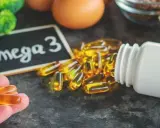 Dłoń trzyma kapsułki z kwasem omega 3. Obok leży buteleczka i tabliczka z napisem "Omega 3".