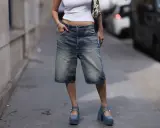 A person in denim bermuda shorts and a white crop top sports chunky blue platform Mary Janes, a nod to early 2000s shoe trends.