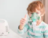 Chłopiec z gorączką i przyspieszonym oddechem używa nebulizatora, pokazując kciuk w górę.