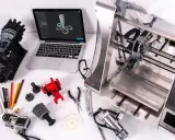 Il disegnatore CAD lavora su un laptop con un modello 3D, circondato da componenti stampati in 3D e strumenti.