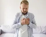 Mężczyzna z rękami na klatce piersiowej, cierpiący z powodu odbijania po jedzeniu.