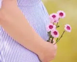 Delikatne kwiaty w dłoni na tle sukienki w paski. To początek pięknej podróży, może właśnie 3 tydzień ciąży.