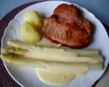 Ein Teller mit gebratenem Schinken, Kartoffeln und Spargel in Sauce Hollandaise. Der Spargel ist in Alufolie gewickelt.