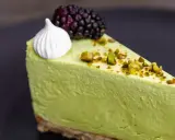 Pyszny sernik pistacjowy na zimno, udekorowany pianką, jeżyną i posypany pistacjami.