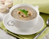 Un réconfortant velouté de champignon, garni de lamelles et d'une touche de persil, servi dans une tasse blanche sur une serviette verte.