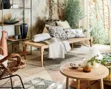 Un salon sans canapé, avec un banc tressé, des coussins décoratifs, un fauteuil en rotin et une étagère murale.