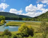 Paisaje de lagunas y montañas verdes, ideal para rutas senderismo Cuenca. Cielo azul con nubes blancas.